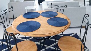 A living room with a blue sofa, a round wooden table with blue placemats, and a hanging wicker chandelier.