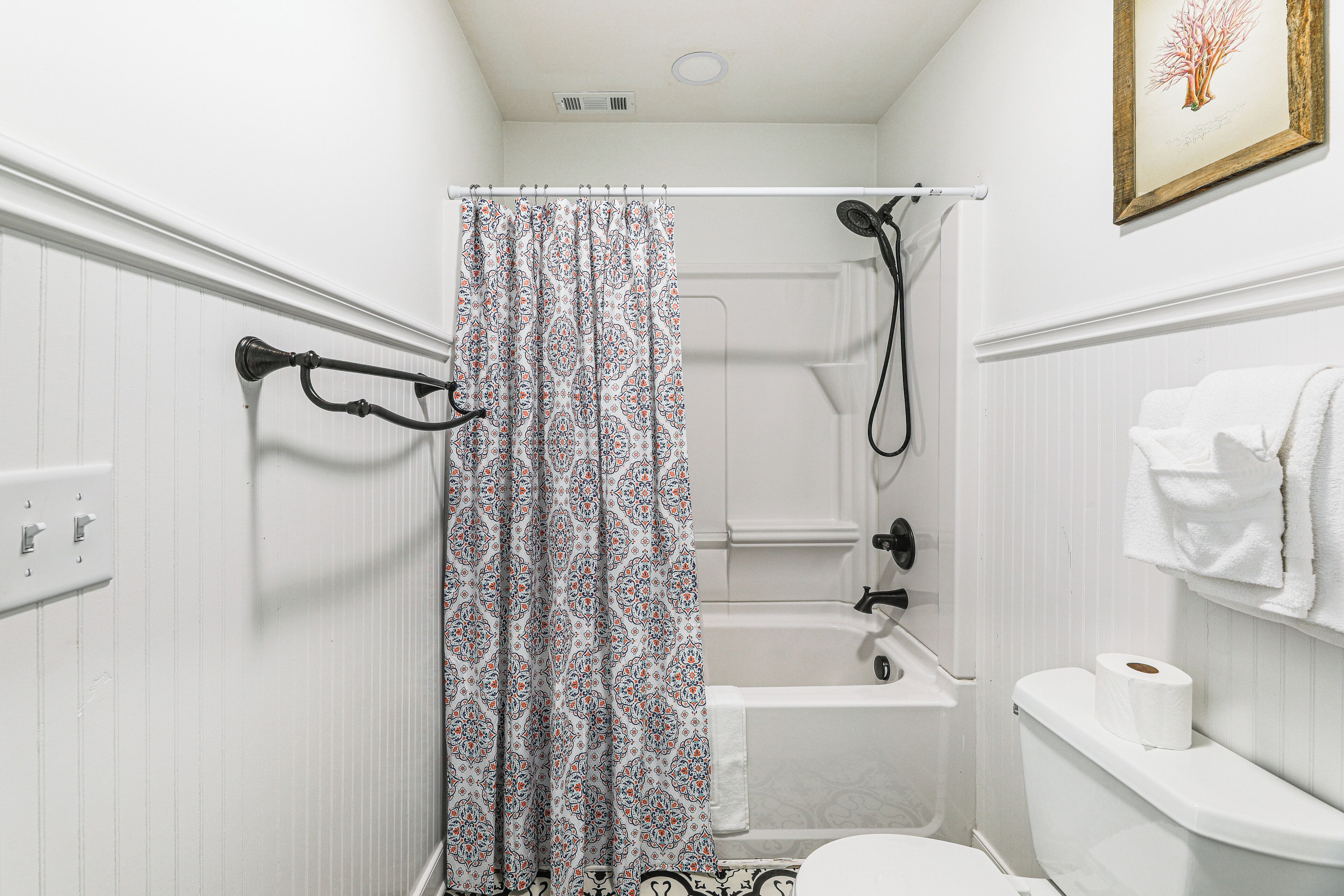 A bathroom with a shower curtain, a bathtub, a toilet, and a towel rack.