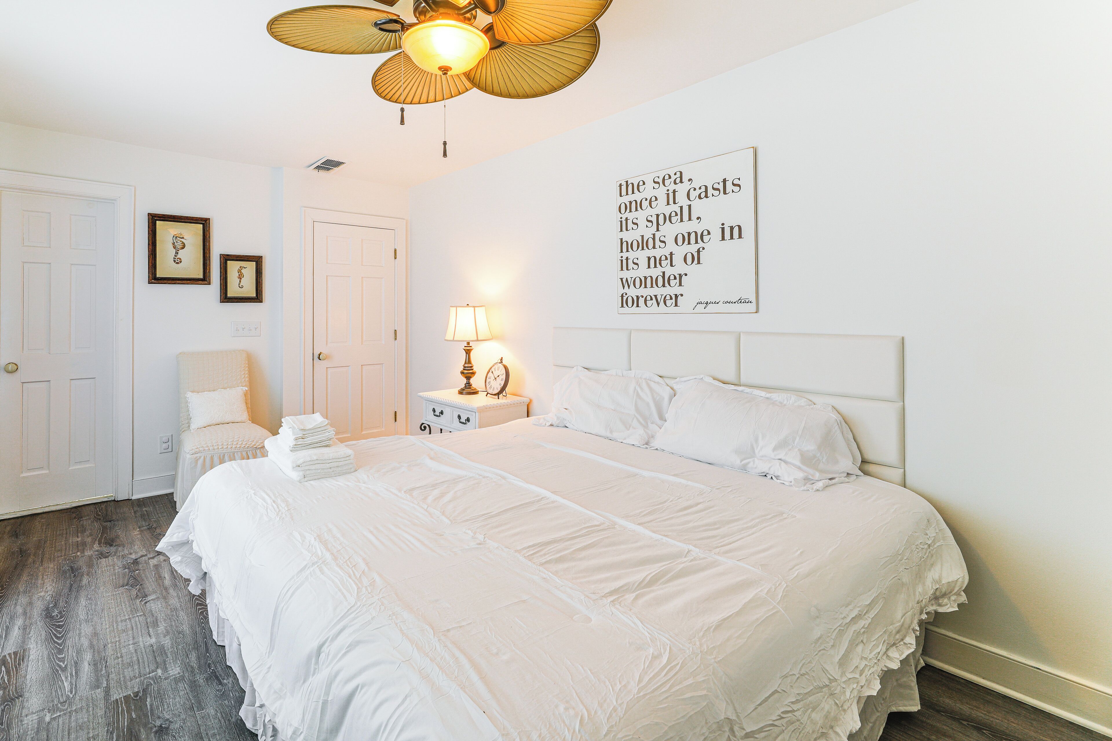 A neatly arranged bedroom with a large bed, a bedside table with a lamp, and a ceiling fan.