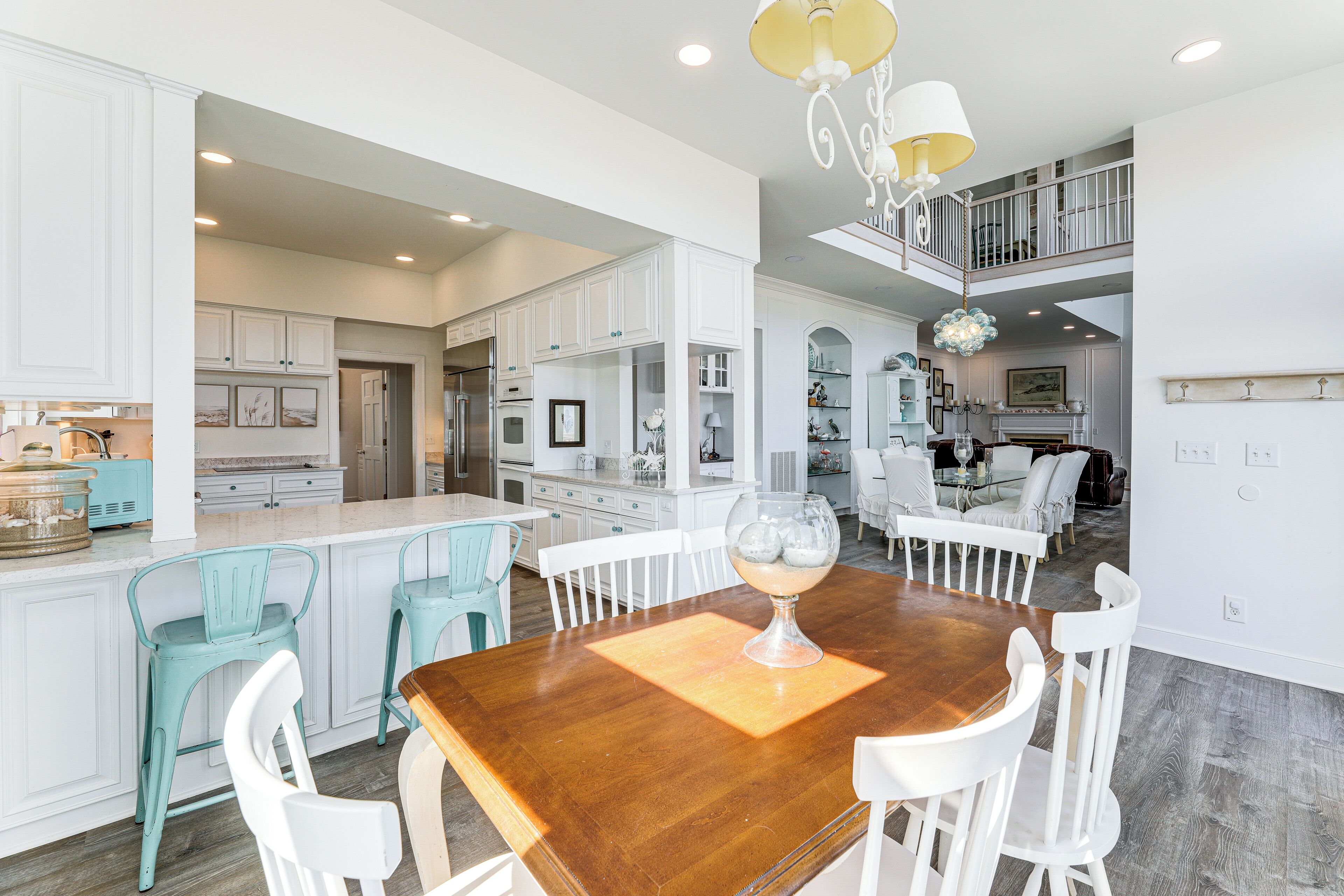 A spacious kitchen with white cabinets, a wooden dining table, and teal chairs.