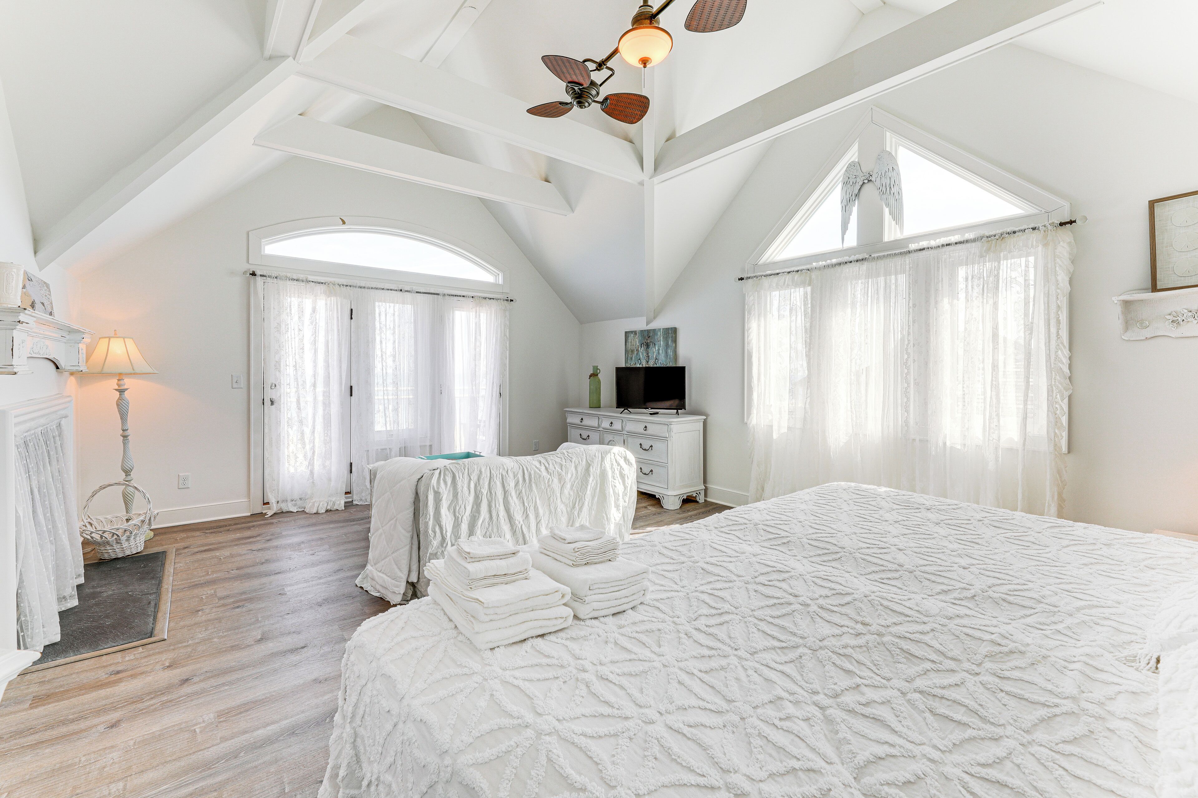 A spacious bedroom with a large bed, a dresser, a television, and a ceiling fan.