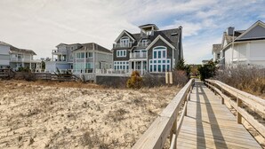 Una propiedad frente a la playa con un paseo marítimo de madera que conduce a una casa grande con varios balcones y un porche cubierto.