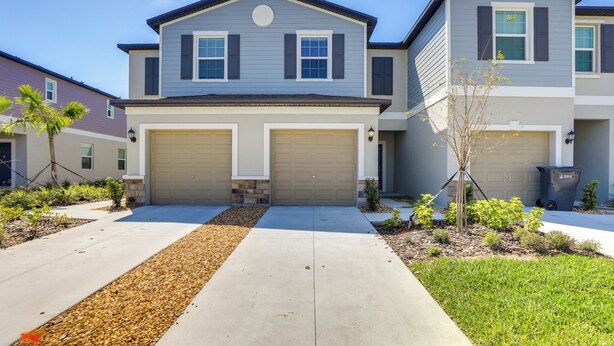 A two-story residential building with a central garage door, a small front yard with landscaping, and a clear blue sky.