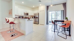A modern kitchen with white cabinets, a central island, and a dining area with bar stools.