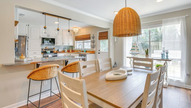 A spacious kitchen with white cabinets, a large island, and hanging wicker pendant lights.