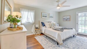 A bedroom with a bed, a ceiling fan, a window with curtains, and a nightstand with a lamp.