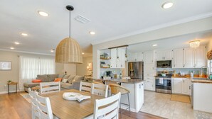 A modern kitchen with white cabinets, a central island, and a dining area with a wooden table and white chairs.