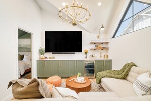 Un salon moderne avec un téléviseur à écran plat, des meubles de rangement verts, une table basse en bois et une grande fenêtre.