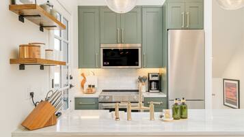 A modern kitchen with green cabinets, stainless steel appliances, and wooden shelves.