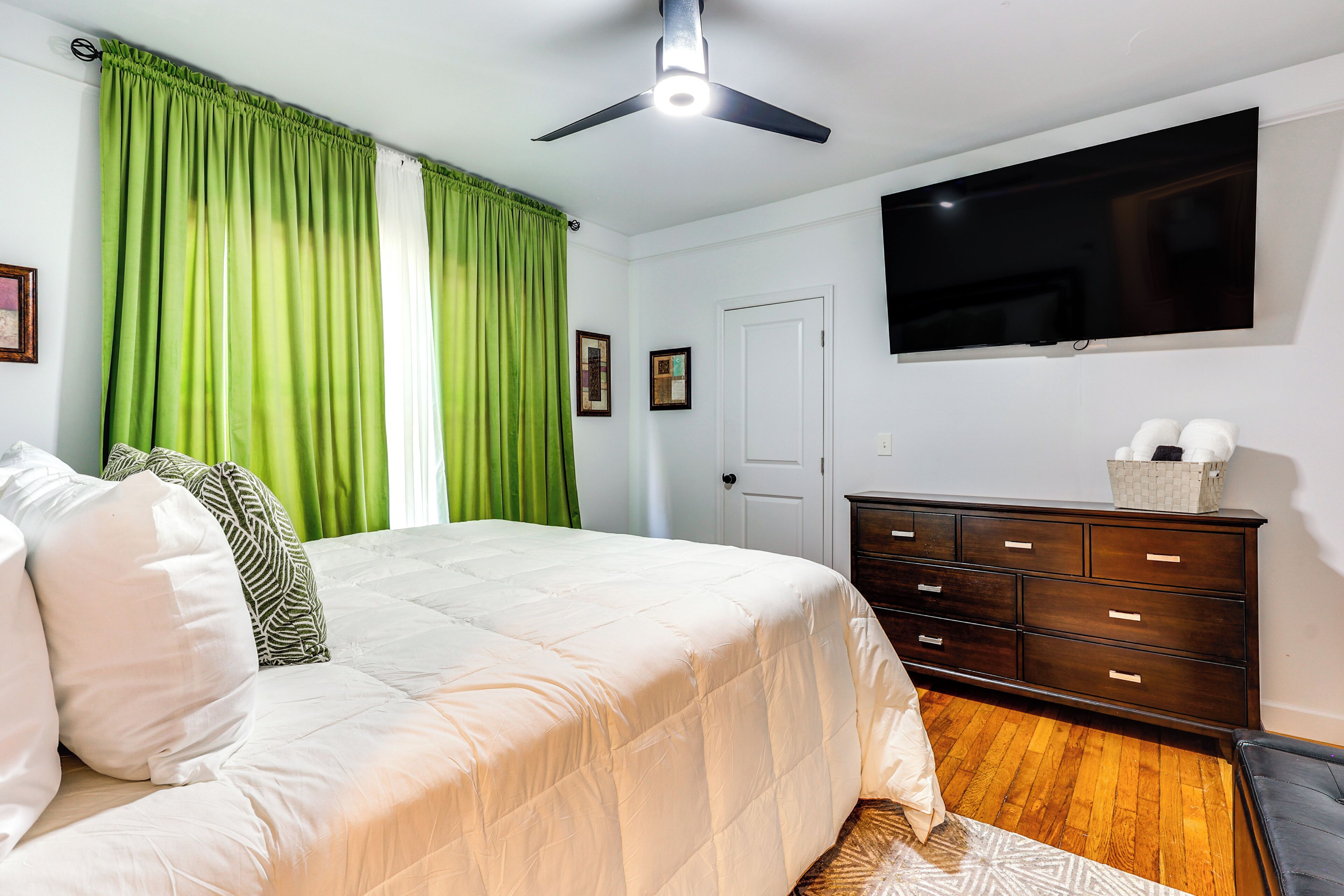 Une chambre à coucher avec un lit, une commode, un ventilateur de plafond, un téléviseur et une porte.