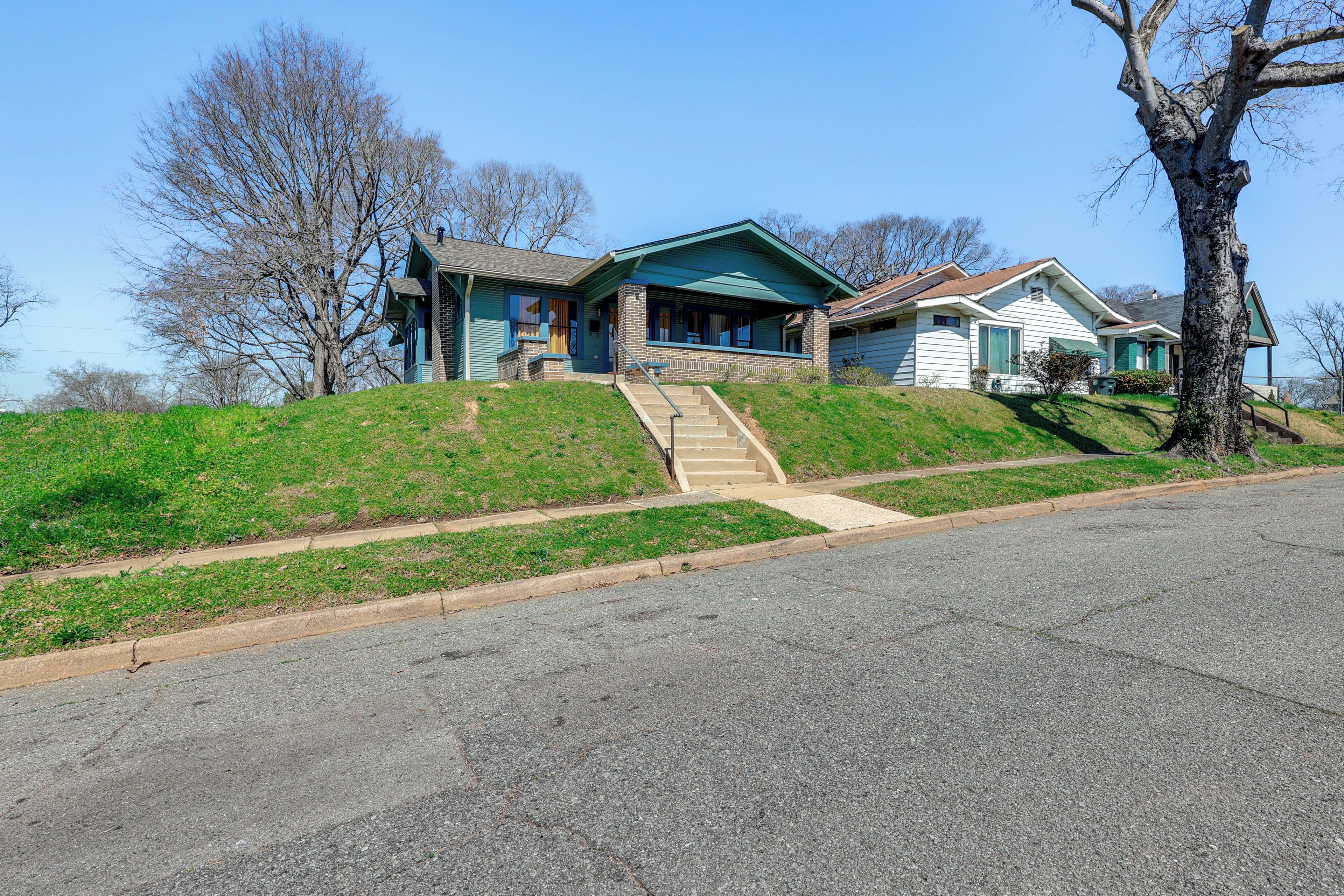 A two-story house with a front porch, a driveway, and a grassy hill.