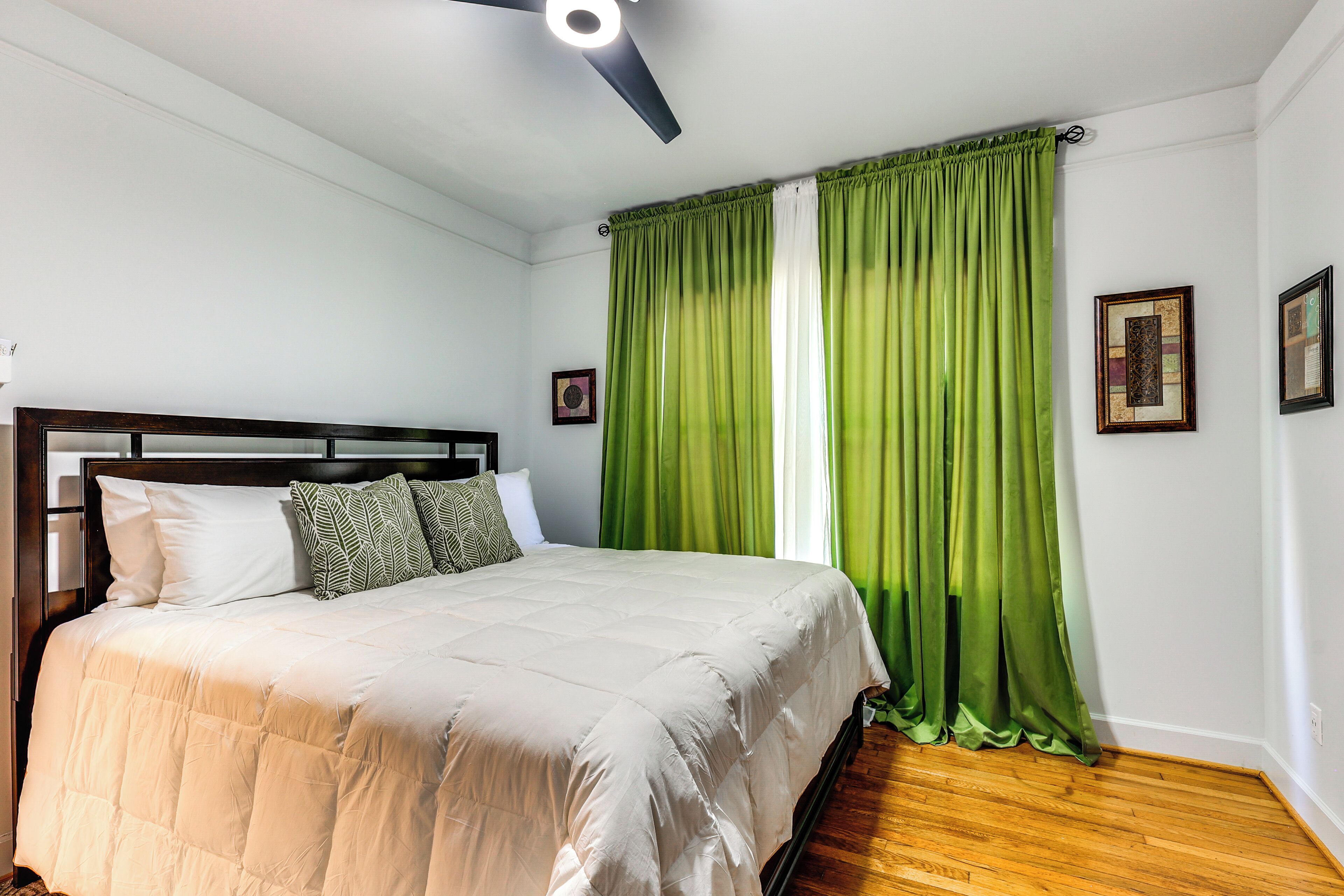 Una camera da letto con un letto, una ventola a soffitto, tende verdi e quadri appesi al muro.