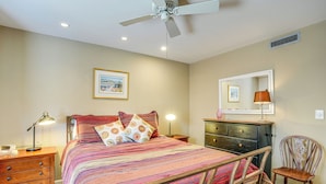 Une chambre à coucher comprenant un lit, une table de chevet, une commode, une chaise et un ventilateur de plafond.