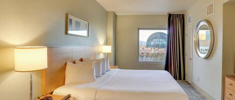 A hotel room with a large bed, a nightstand with a lamp, a dresser, and a window with curtains.