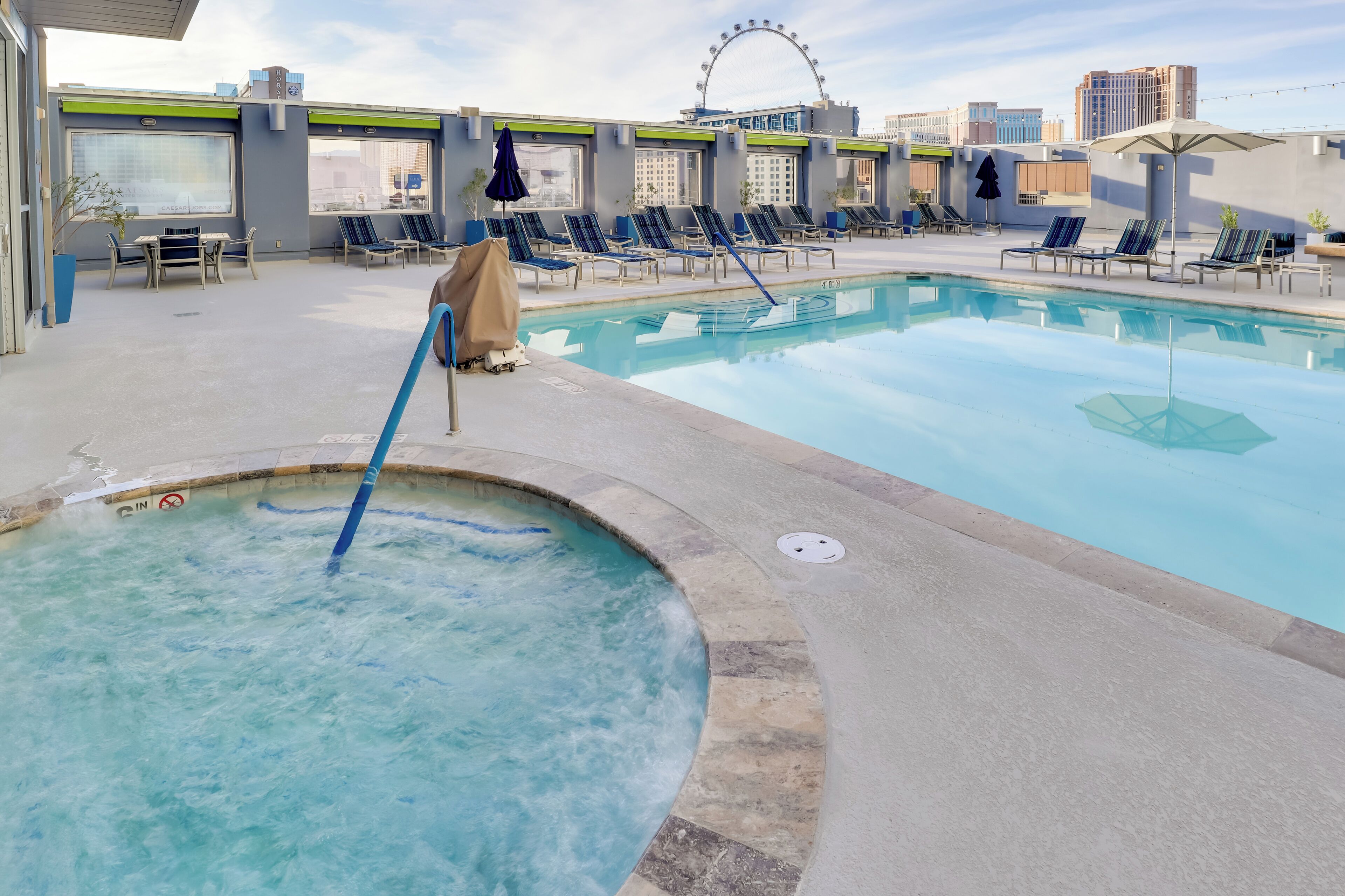 A pool area with lounge chairs, a hot tub, and a Ferris wheel in the background.