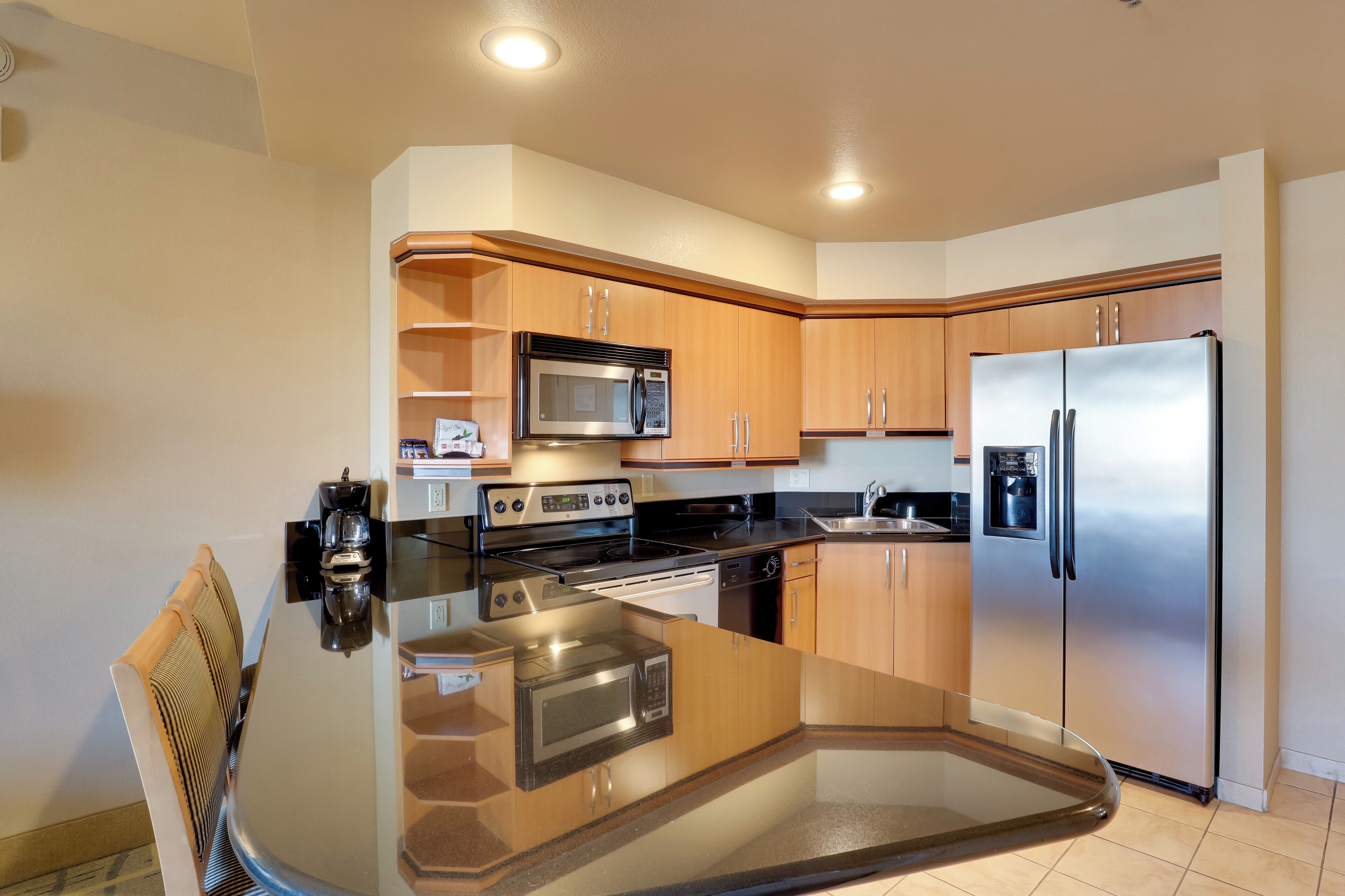 A modern kitchen with wooden cabinets, stainless steel appliances, and a glass dining table.