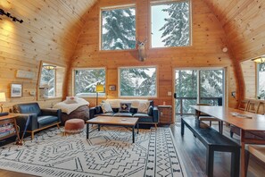 L’intérieur d’un chalet confortable, avec un plafond en bois, de grandes fenêtres, un canapé, une table basse et une table à manger.