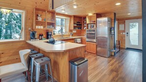 A modern kitchen with wooden walls, stainless steel appliances, and a bar area. - Hot Tub & Sauna: Mountain Living at Hyak Cabin! (Snoqualmie Pass)