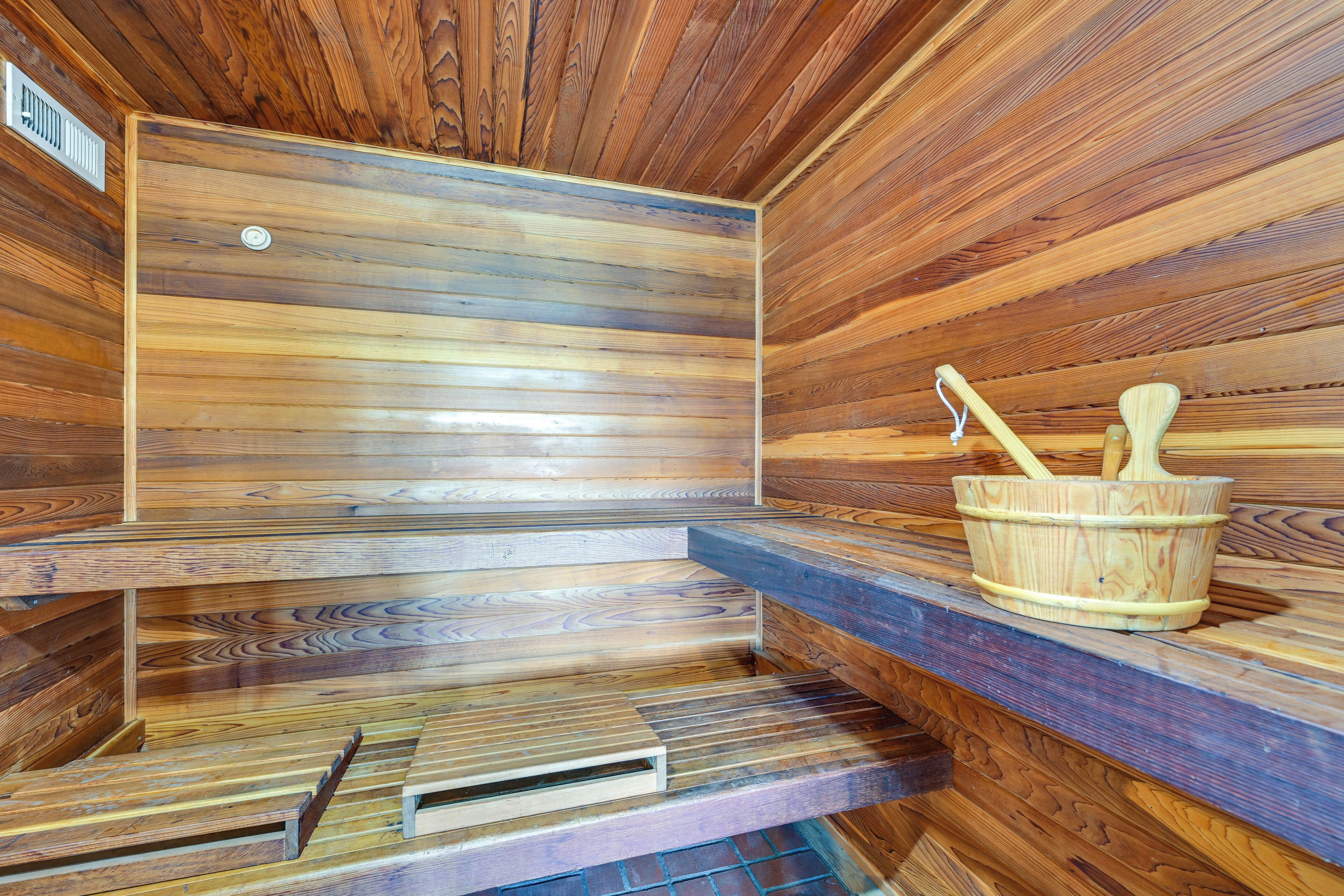 A sauna with wooden walls and benches, a wooden bucket with a brush, and a ventilation vent.