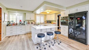 A modern kitchen with white cabinetry, a large island with stools, a stainless steel refrigerator, and a microwave. - 9 Mi to Spanaway Park: Home w/ Indoor Hot Tub (Spanaway)