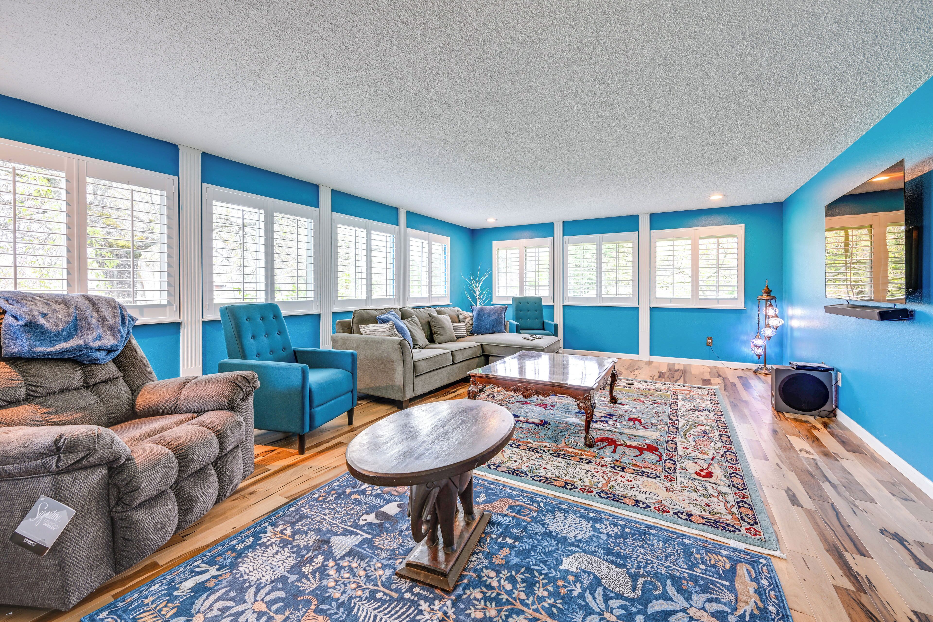 Un salón espacioso con una pared azul de acento, ventanas amplias, un sofá, sillones y una mesa de centro.