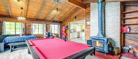 A pool table in a wooden room with a fireplace and a bench.