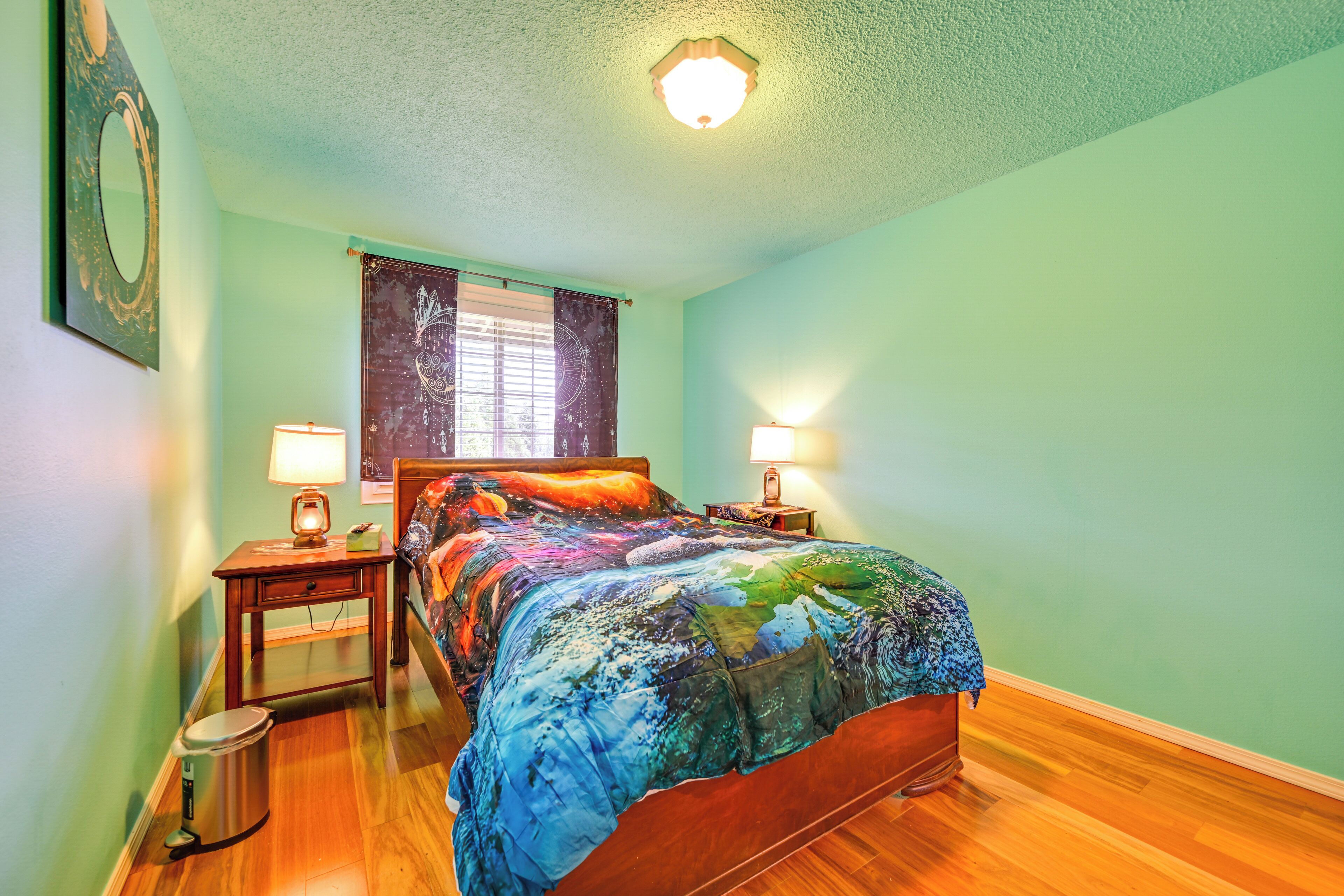 A bedroom with a wooden bed, two bedside tables with lamps, a nightstand, a trash bin, and a window with curtains.