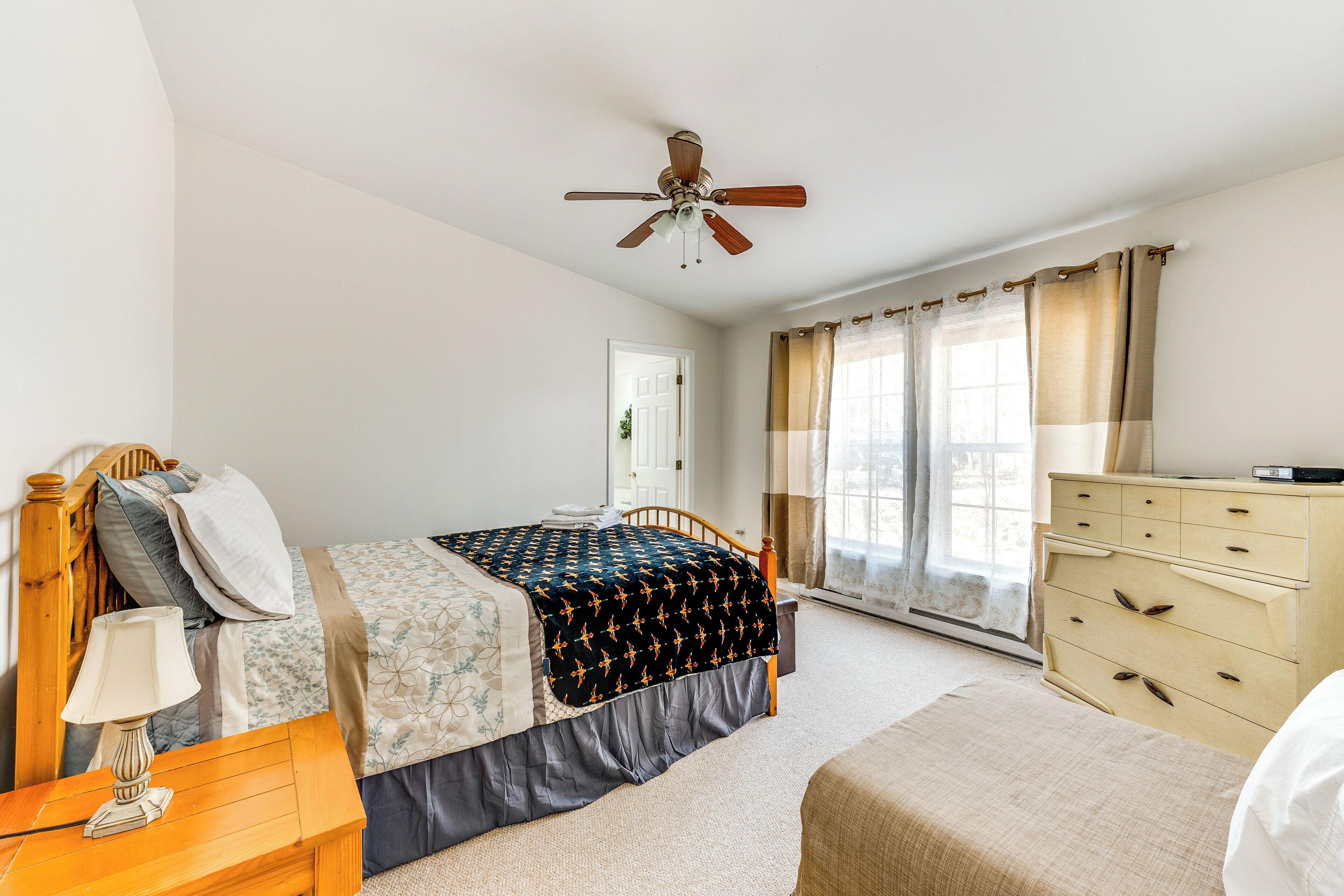 A bedroom with a bed, a nightstand, a dresser, a ceiling fan, and a window with curtains.
