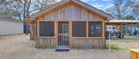A wooden cabin with a porch, large windows, and a gravel driveway.