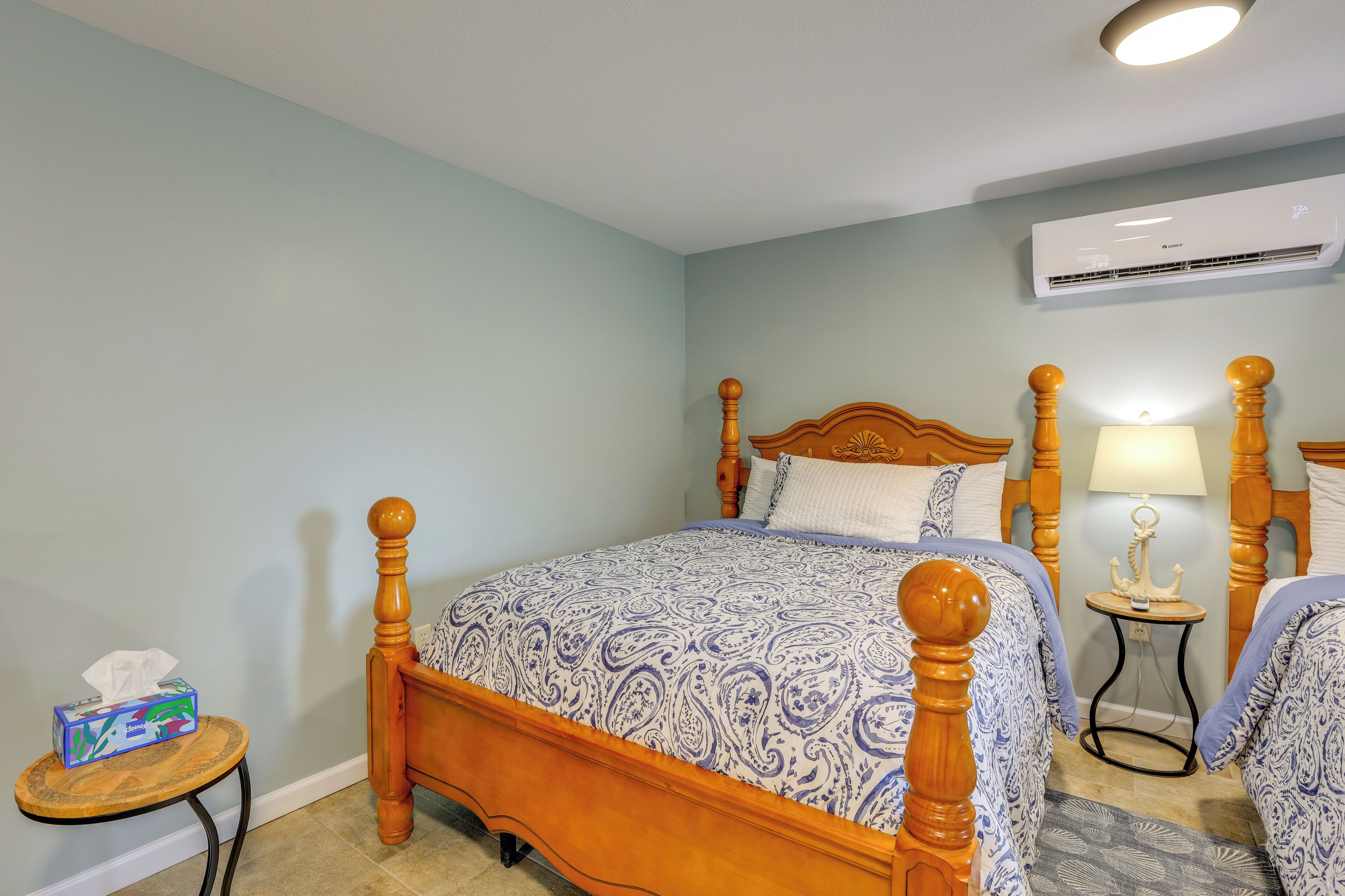 A bedroom with a wooden four-poster bed, a bedside table with a lamp, and an air conditioning unit on the wall.