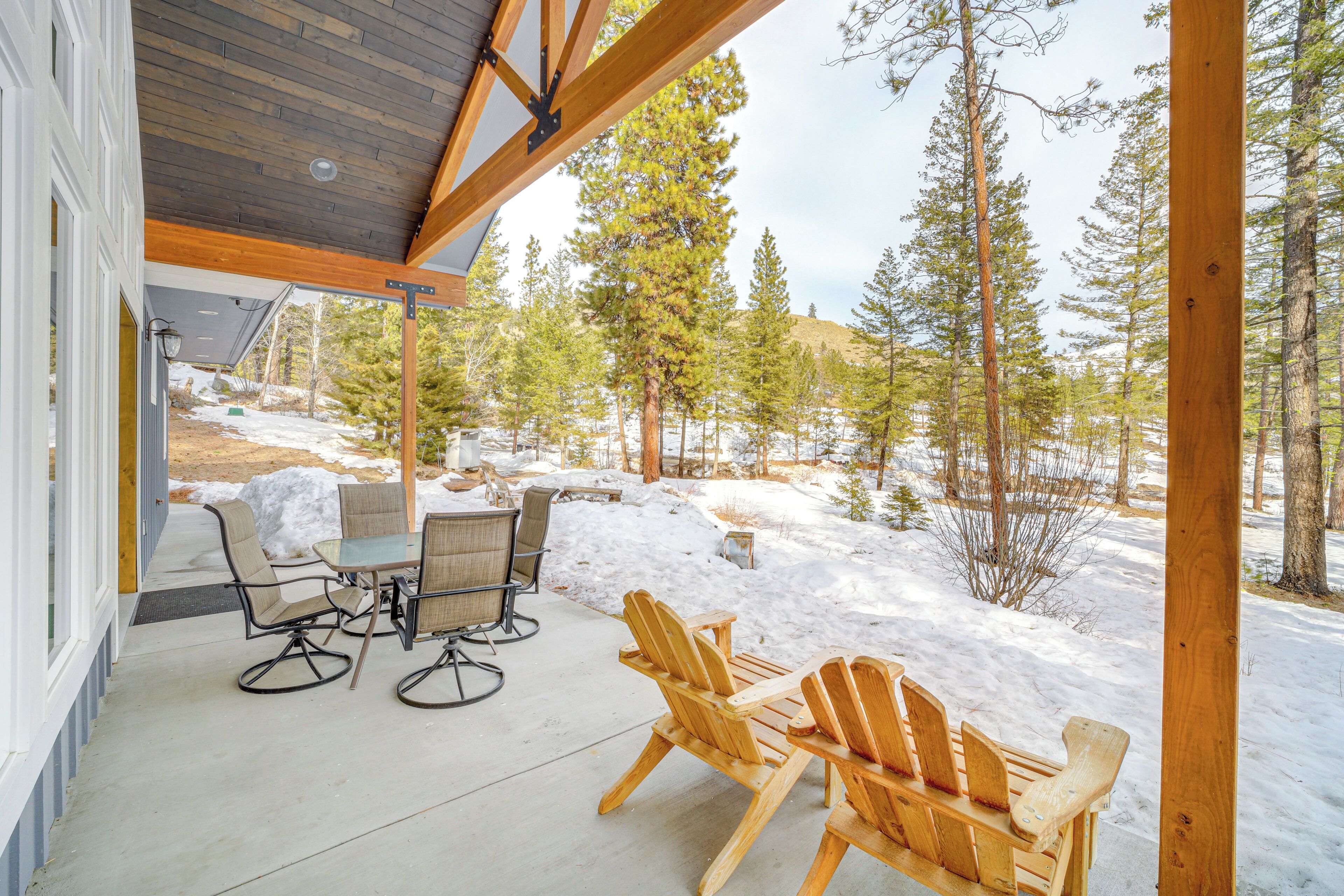 A covered patio with a table and chairs, overlooking a snowy landscape with trees.