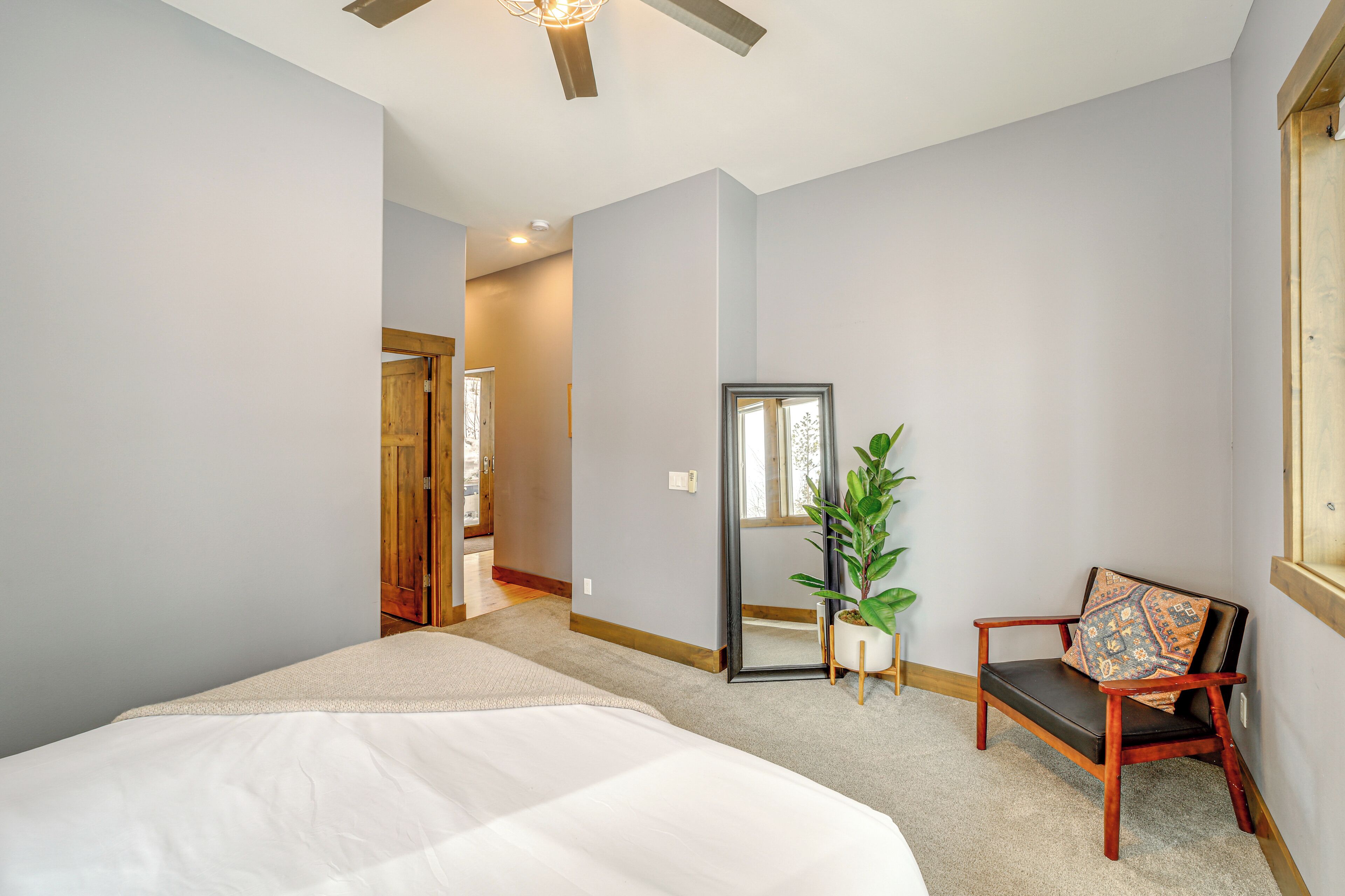 Une chambre à coucher avec un grand lit, une chaise en bois, une plante en pot et un miroir accroché au mur.
