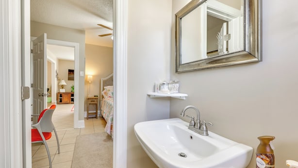 Une salle de bain avec un lavabo blanc, un miroir et une étagère contenant des articles de toilette.