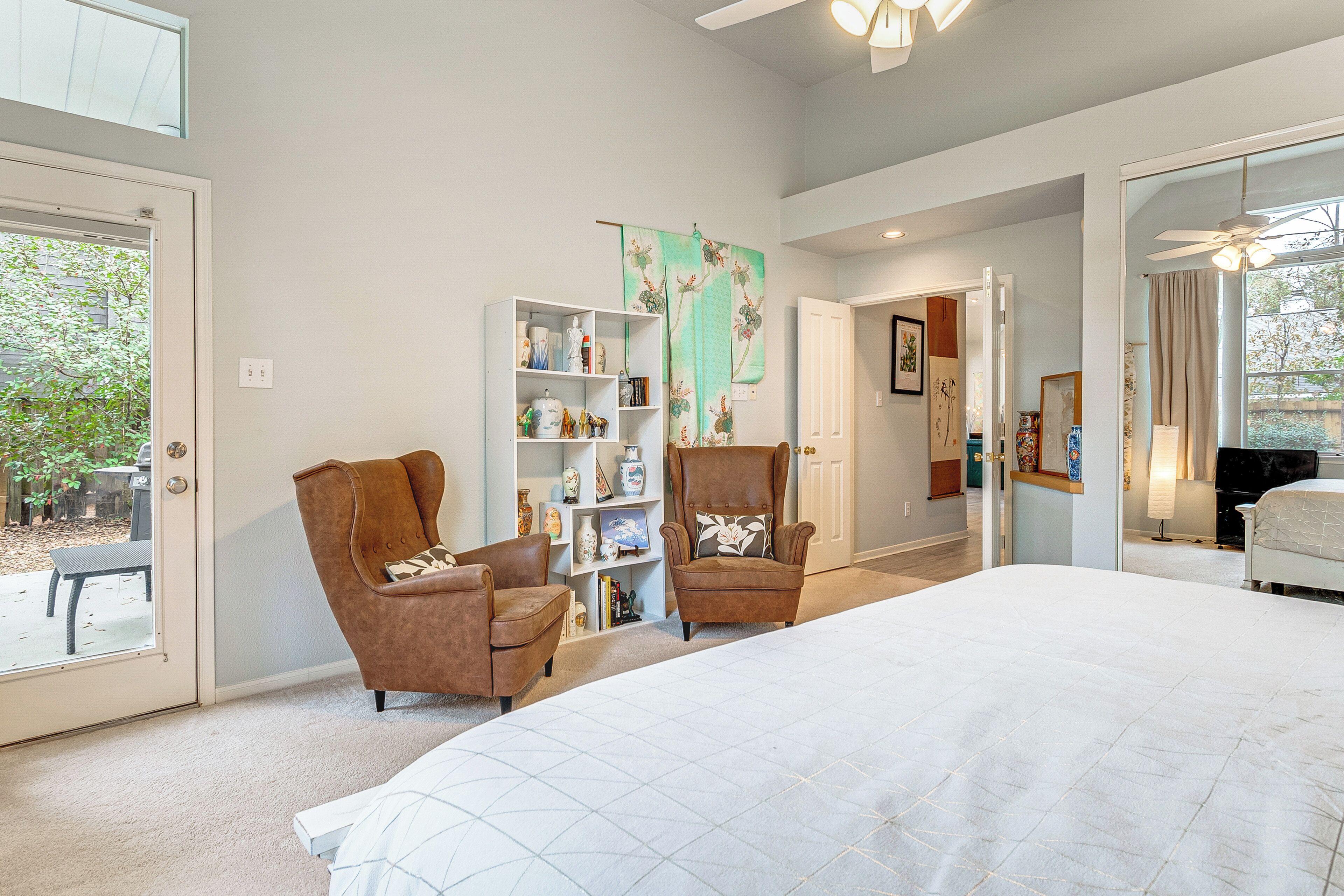 Un dormitorio con una cama grande, dos sillones, una estantería y una puerta que da a otra habitación.