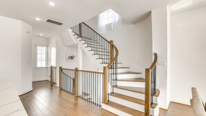A spacious room with a wooden staircase, white walls, and a large window. - 7 Mi to The Galleria: Modern Home w/ Fenced Yard (Houston)