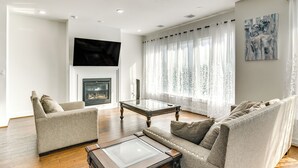 A living room with a fireplace, two sofas, a coffee table, and a TV mounted on the wall. - 7 Mi to The Galleria: Modern Home w/ Fenced Yard (Houston)