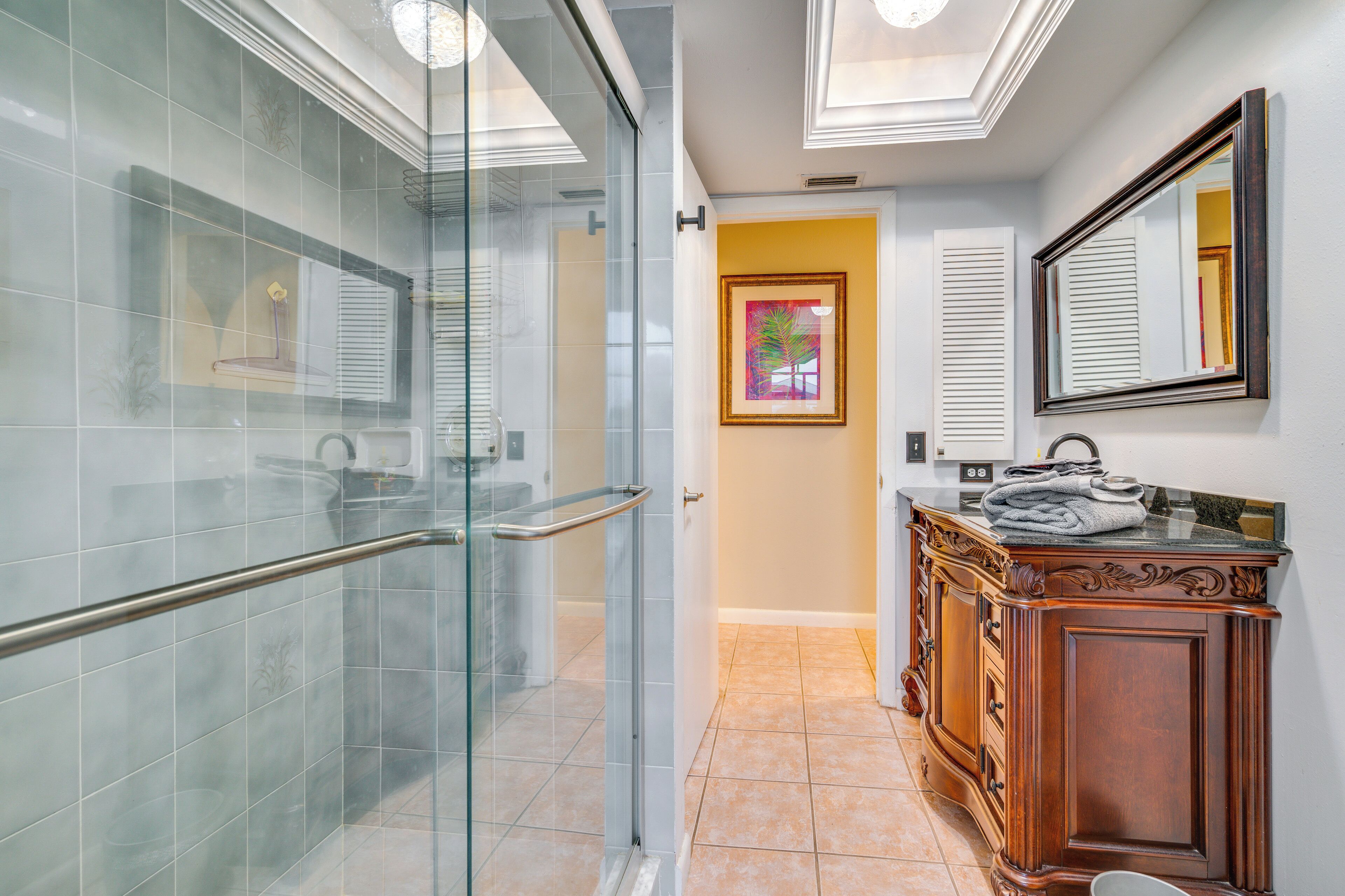 A modern bathroom with a glass shower, a wooden vanity, and a framed artwork on the wall.