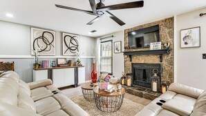 A modern living room with a sectional sofa, a fireplace, a flat-screen TV, and a ceiling fan. - 4 Mi to Airport: Atlanta Home w/ Deck & Hot Tub (Atlanta)