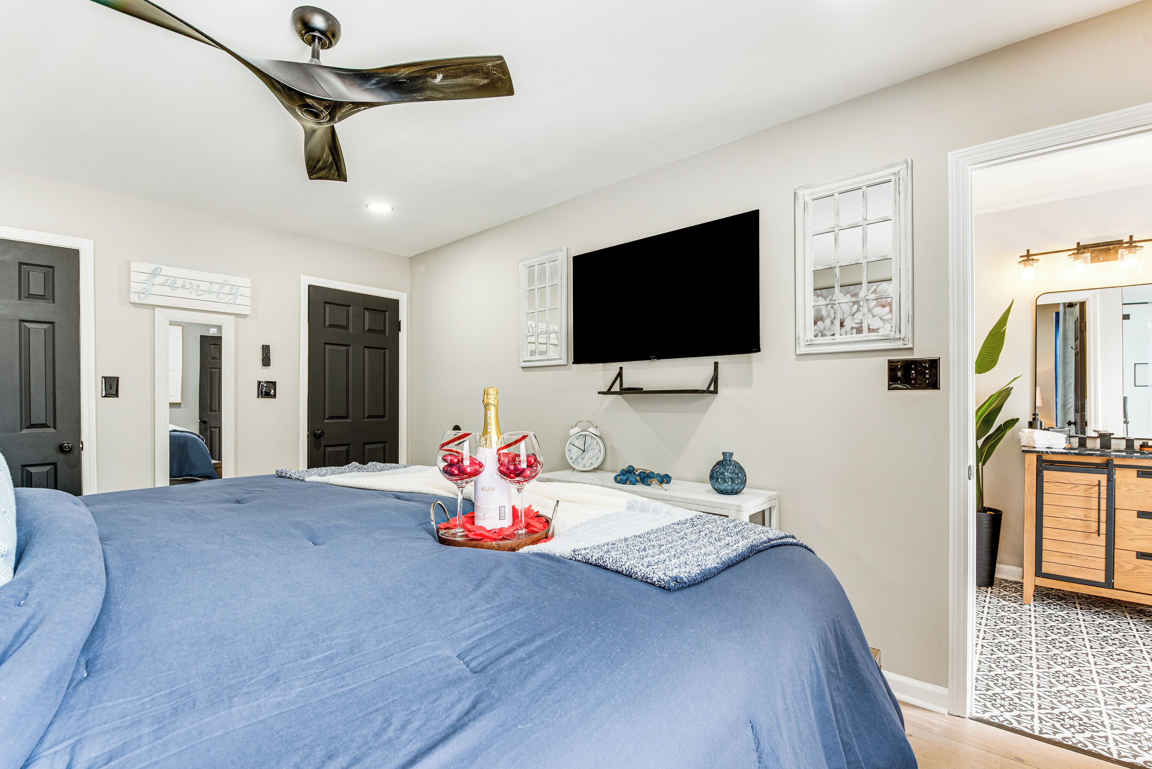 Une chambre à coucher comprenant un lit, un téléviseur à écran plat, une table de chevet, une commode et une porte.