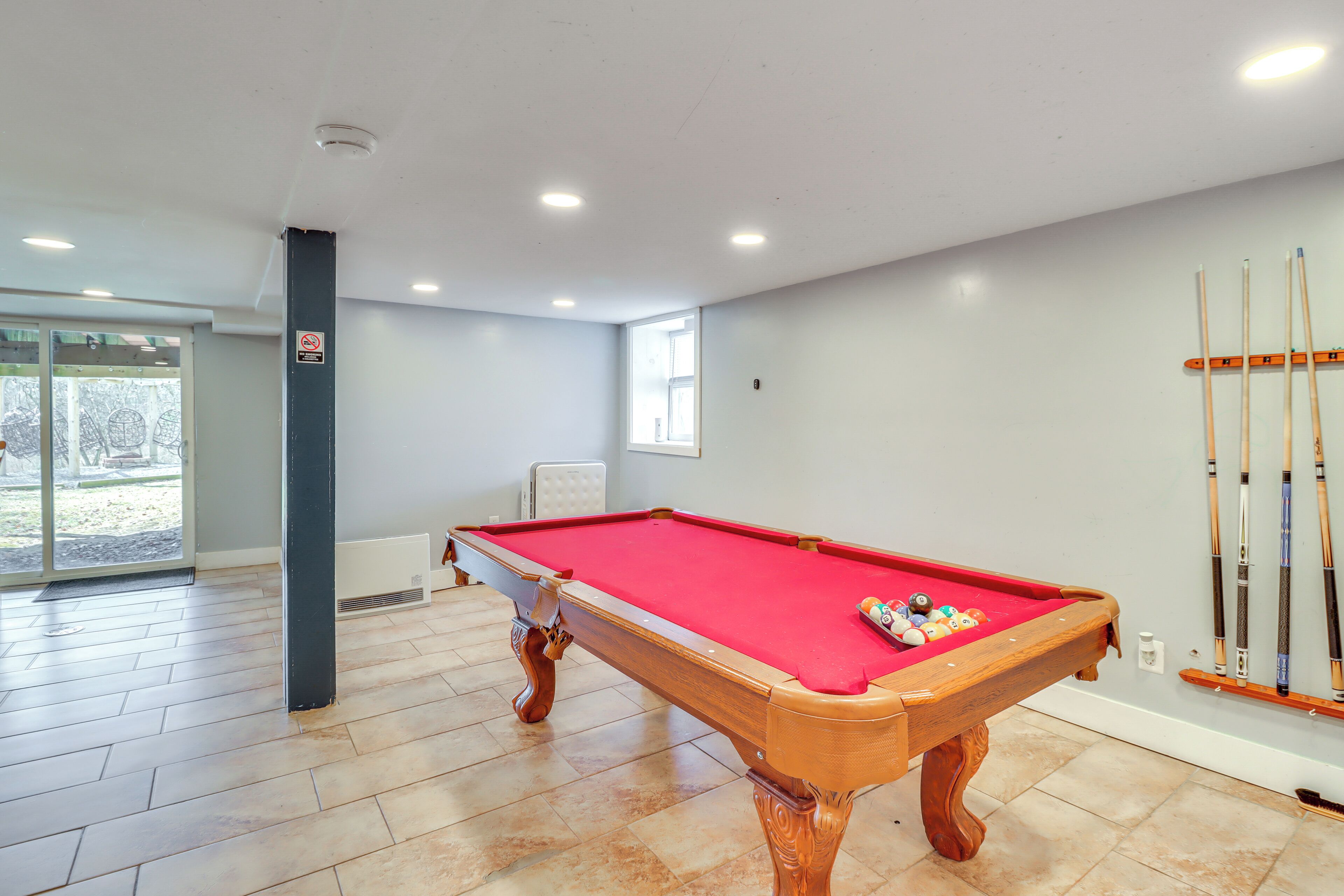 A pool table with a red felt surface, a white ceiling, and a window in the background.