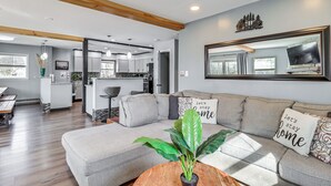 Un salon moderne avec un canapé gris, des poutres en bois, un grand miroir et une plante en pot.