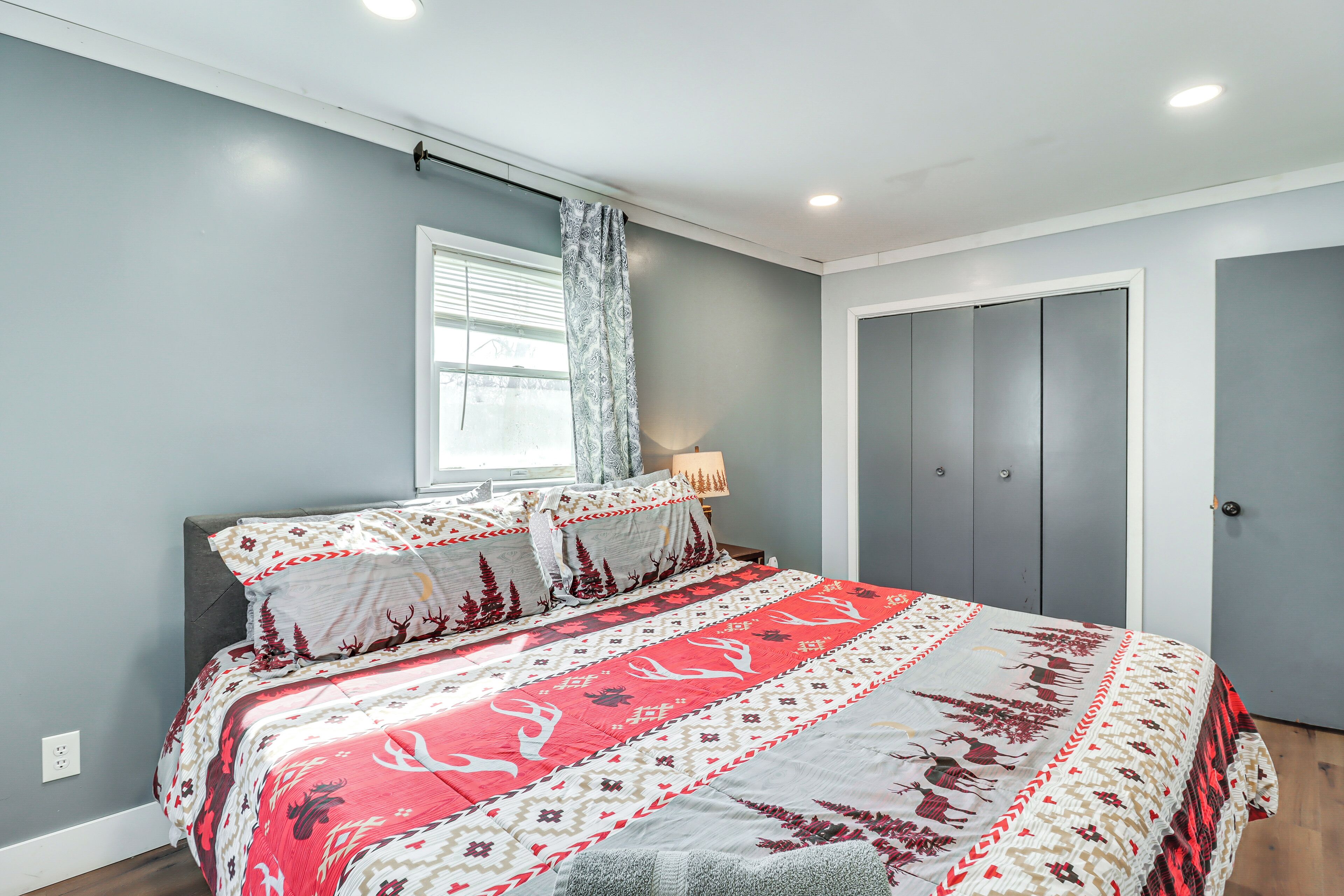 A bedroom with a bed, a window with curtains, a door, and a nightstand with a lamp.