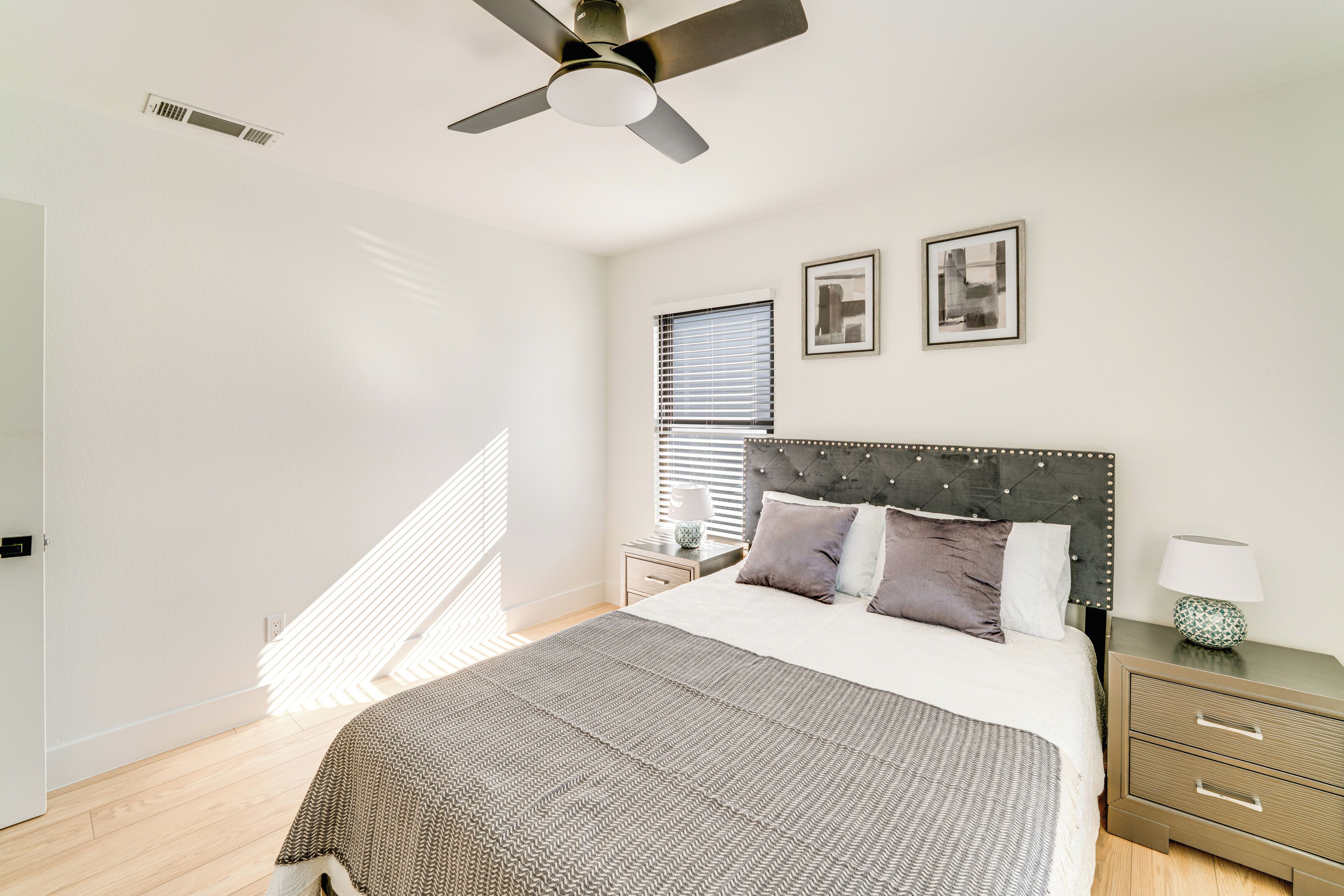 A bedroom with a bed, a nightstand, a lamp, a ceiling fan, and a window with blinds.