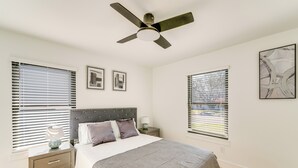 A bedroom with a bed, nightstands, a ceiling fan, and two windows with blinds.