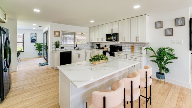 A modern kitchen with white cabinets, a marble island, and bar stools.