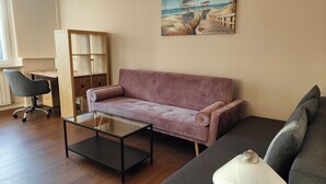 A living room with a sofa, a glass coffee table, a desk, and a lamp.
