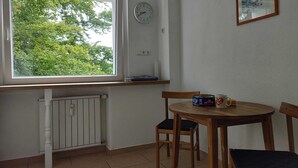 A small room with a window, a clock, a framed picture, and a table with chairs.