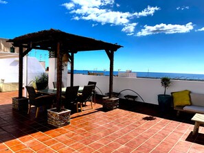 A terrace with a pergola, outdoor furniture, and a view of the sea.