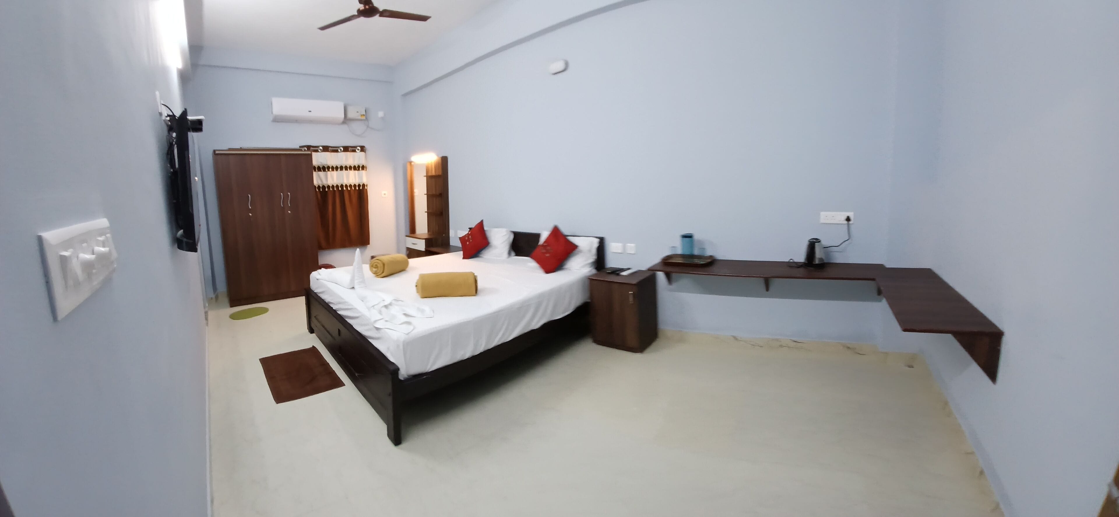 A bedroom with a bed, bedside table, wardrobe, and a desk with a chair.