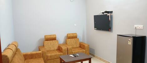 A living room with a sofa, two armchairs, a coffee table, a flat-screen TV, and a refrigerator.